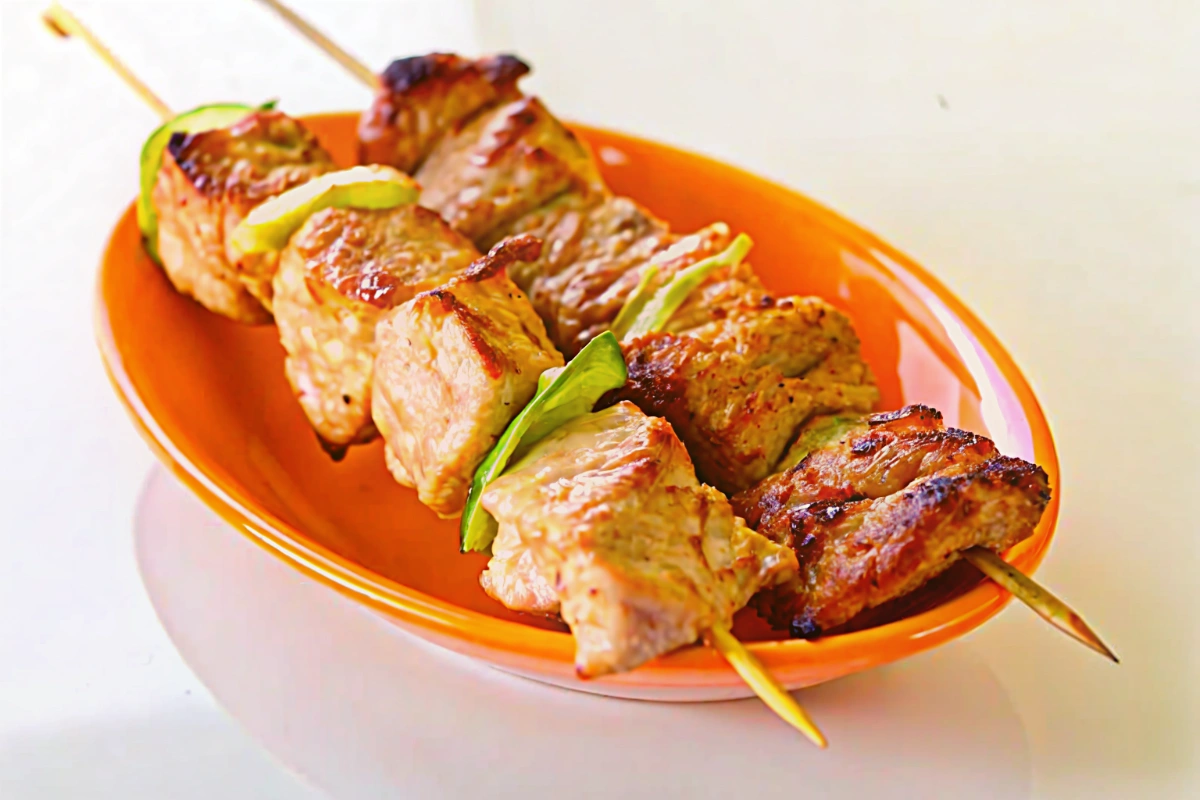 Chich taouk servi sur une planche en bois, accompagné de pitas, salade et yaourt, en soirée douce lumière